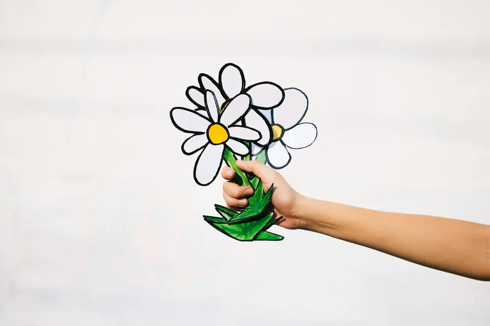 Hand holding a drawn flower against pale light.