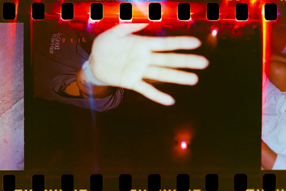 Blurred hand across dark film-frame light leaks.