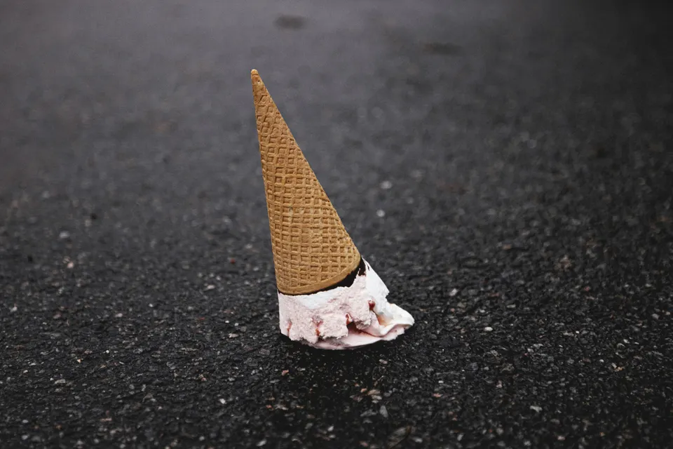 Melting ice cream cone on dark asphalt.