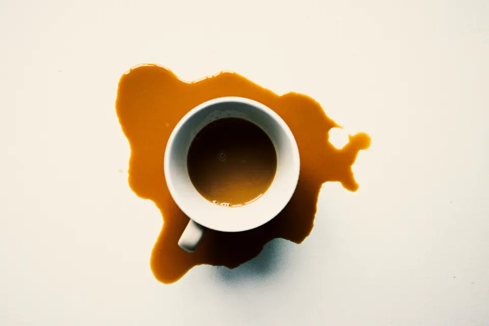 Coffee cup casting a hard shadow on a spill of coffee.